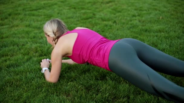 En kvinnlig idrottare pumpar musklerna i pressen. Sexig tjej är engagerad i fitness i parken. — Stockvideo
