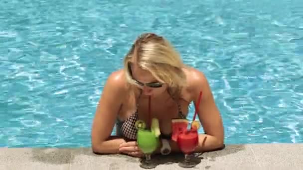 Een mooie vrouw in een zwembad drankjes tropische cocktails. — Stockvideo