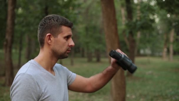 Un joven mira a través de prismáticos. Un tipo con prismáticos contra los árboles . — Vídeos de Stock