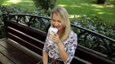 Bir kız dışında çay içiyor. Güzel kadın bankta kahve içiyor.