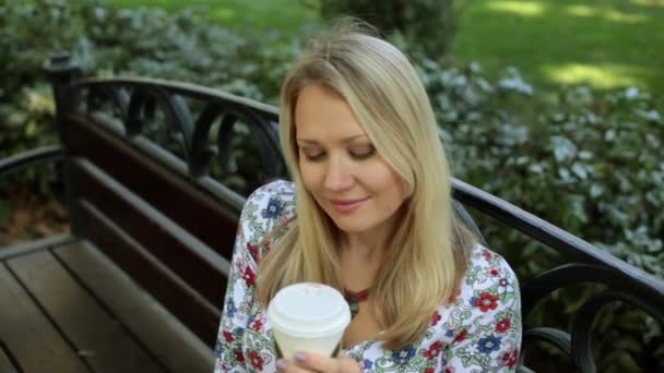 Hermosa joven está bebiendo café en el banco. Una chica está tomando té afuera. . — Vídeo de stock