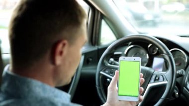 Arabadaki adam yeşil ekrana sahip bir smartphone tutuyor