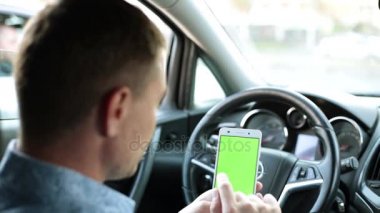 Arabadaki adam bir akıllı telefon ile yeşil bir ekran kullanır..