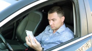 Genç bir işadamı arabada oturmak için bir akıllı telefon kullanır.