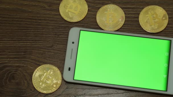 Gyllene bitcoins och smartphone med en grön skärm för ditt innehåll. — Stockvideo