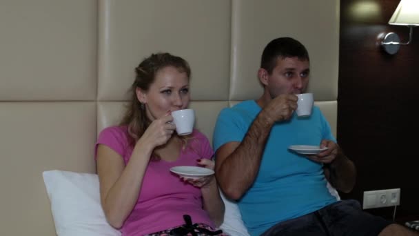 Een man en een vrouw drinken koffie op het bed — Stockvideo