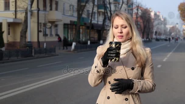 Uma mulher caminha pela rua e bebe café e chá . — Vídeo de Stock