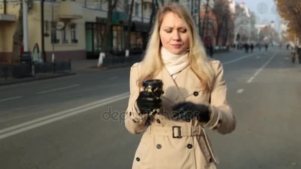 Une femme descend la rue et boit du café et du thé . — Video