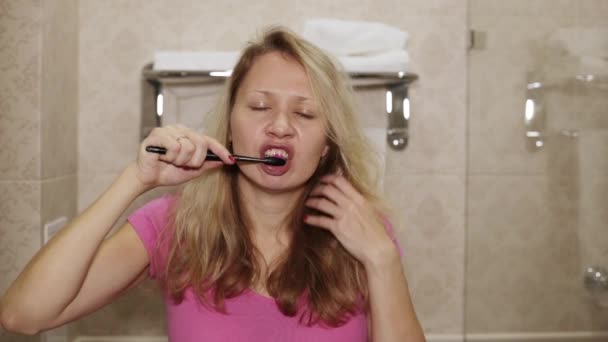 A sleepy woman is brushing her teeth. Young woman brushing her teeth in the bathroom. — Stock Video