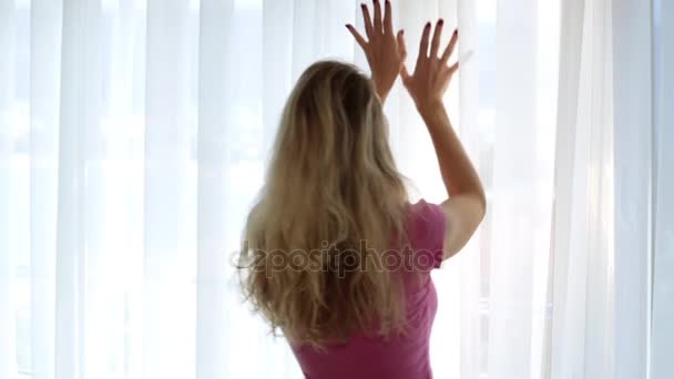 Una joven abre la cortina por la mañana . — Vídeo de stock