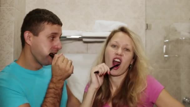 Um homem e uma mulher escovam os dentes na casa de banho. Casal jovem escovando os dentes . — Vídeo de Stock