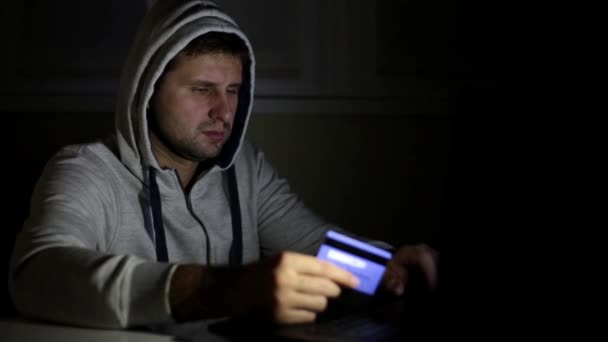 Un hacker con un portátil y una tarjeta bancaria . — Vídeo de stock
