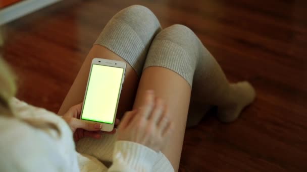 Una mujer se sienta en una habitación y sostiene un teléfono inteligente con una pantalla verde . — Vídeo de stock