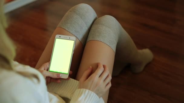 Een vrouw zit in een kamer en het bezit van een smartphone met een groen scherm. — Stockvideo