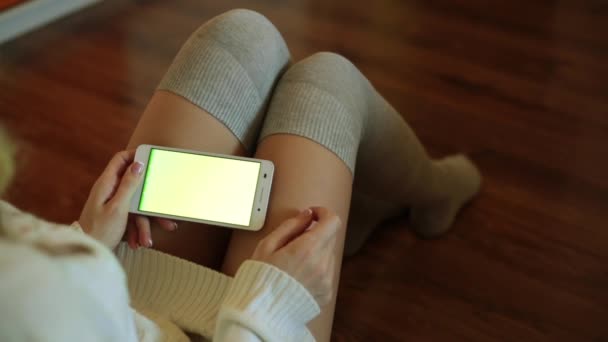 Una hermosa mujer se sienta en una habitación y sostiene un teléfono inteligente con una pantalla verde . — Vídeos de Stock