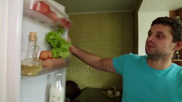 Un hombre saca leche y huevos del refrigerador. Un hombre en la cocina abre la nevera . — Vídeos de Stock