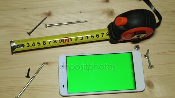 Uno smartphone con display verde, un metro a nastro da costruzione e viti . — Video Stock