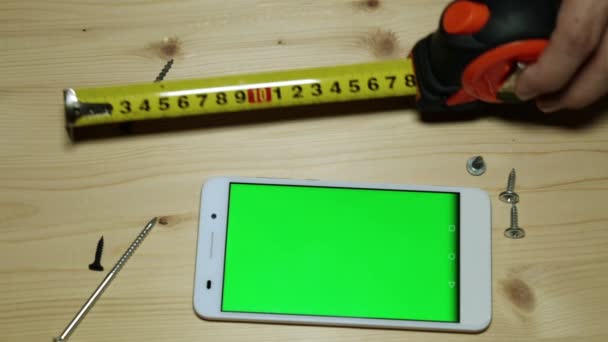 Uno smartphone con display verde, un metro a nastro da costruzione e viti . — Video Stock