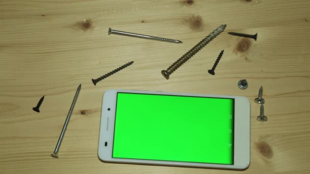 여러분의 컨텐츠를 위한 녹색 화면을 가진 스마트폰이죠. 나무 탁자 위에 놓인 전화기와 나무 나사. — 비디오