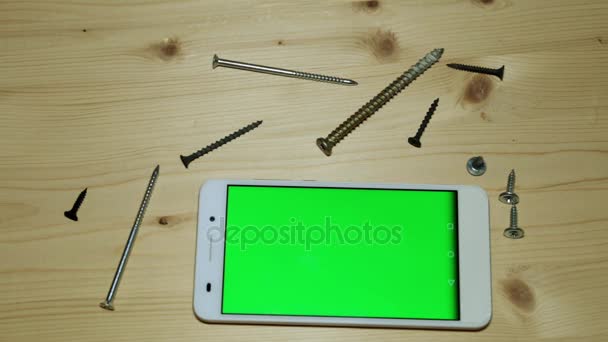 Un smartphone con pantalla verde para tu contenido. Teléfono y tornillos de madera en una mesa de madera. — Vídeo de stock