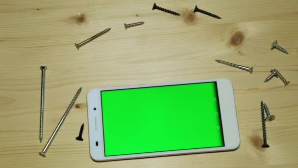 Uno smartphone con schermo verde, un coltello da costruzione, un cutter e viti . — Video Stock