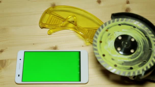 Uno smartphone con schermo verde e strumenti di costruzione. Occhiali da costruzione e rettificatrice . — Video Stock