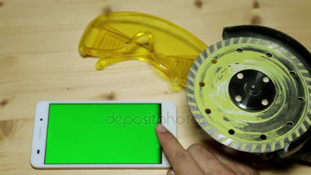Smartphone with a green display and a grinding machine. Telephone and construction tools on the workbench. — Stock Video