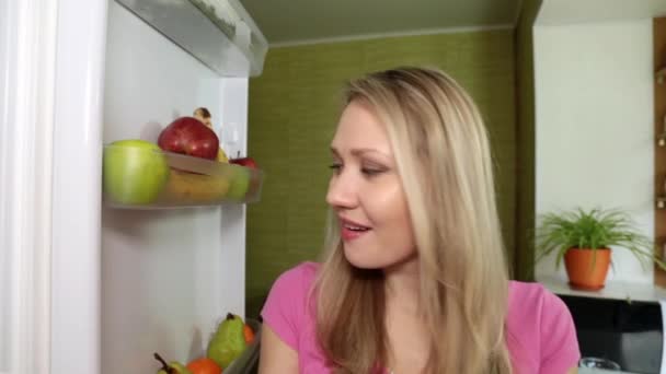 A young woman eats persimmon in the kitchen with pleasure. — Stock Video