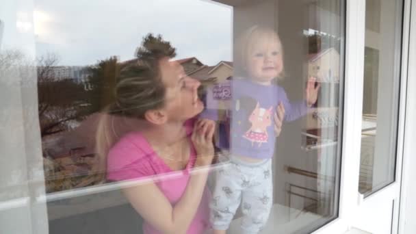 Moeder en baby zoekt uit het raam. — Stockvideo