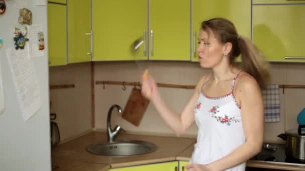 Uma mulher dona de casa ouve música e dança em casa na cozinha . — Vídeo de Stock
