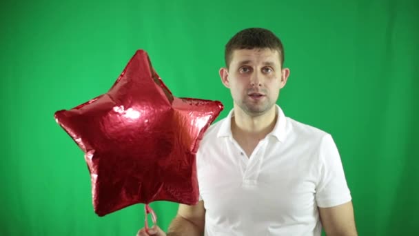 Молодой человек с красным воздушным шаром на зеленом фоне . — стоковое видео