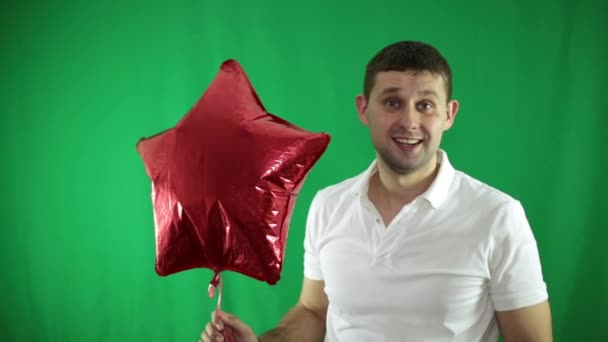 Hombre alegre con un globo de aire rojo sobre un fondo verde . — Vídeos de Stock