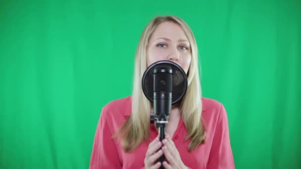 Een jonge vrouw zingt in een microfoon op een groene achtergrond. — Stockvideo