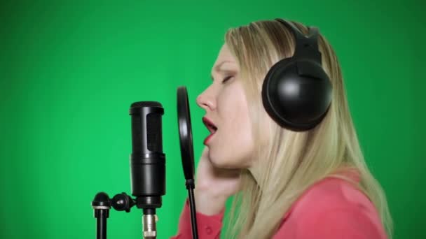 Retrato de una mujer cantando en un micrófono sobre un fondo verde . — Vídeo de stock