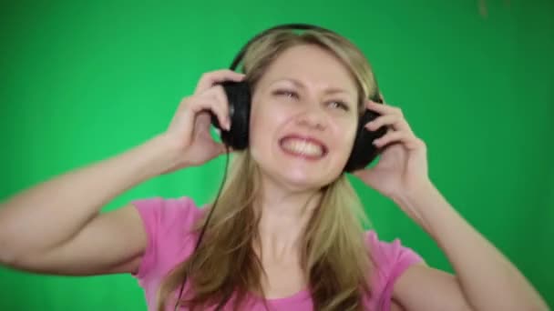 Jonge vrouw, luisteren naar muziek op de hoofdtelefoon op een groene achtergrond. — Stockvideo