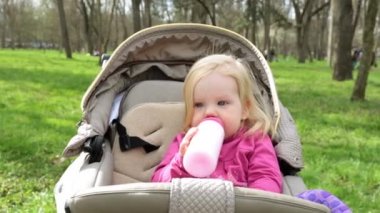 Bir çocuk arabasındaki bebek yiyor ve bir şişeden içer.