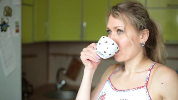 Una giovane donna sta bevendo tè o caffè in cucina . — Video Stock