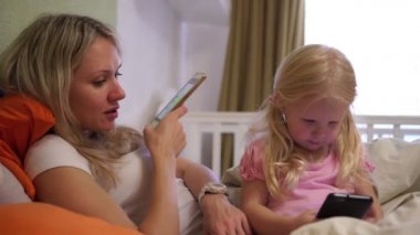 Anne ve küçük kızı evde akıllı telefon kullanıyor. Yatakta yatıyor..