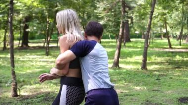 Spor giyimli genç bir kadın bir dövüş sanatları eğitmeniyle parkta antrenman yapıyor..