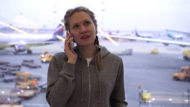 Kvinna turist talar på en smartphone på flygplatsen i bakgrunden av flygplan — Stockvideo