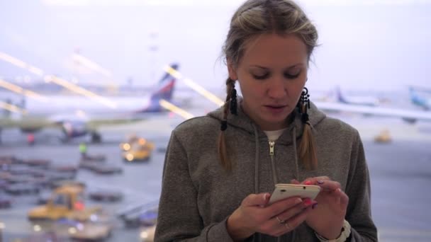 En kvinna använder en smartphone på flygplatsen på en bakgrund av flygplan — Stockvideo