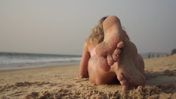 Denizin arka planında kumlu bir sahilde güneşlenen bir kadın. — Stok video