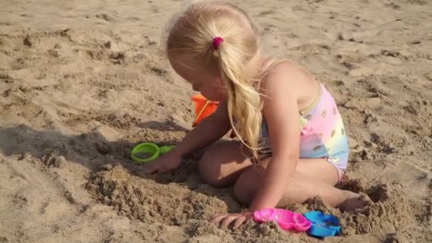 Criança menina loira joga na areia na praia . — Vídeo de Stock