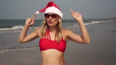 Kırmızı mayolu güzel bir kadın ve kumsalda dans eden Noel Baba şapkası.