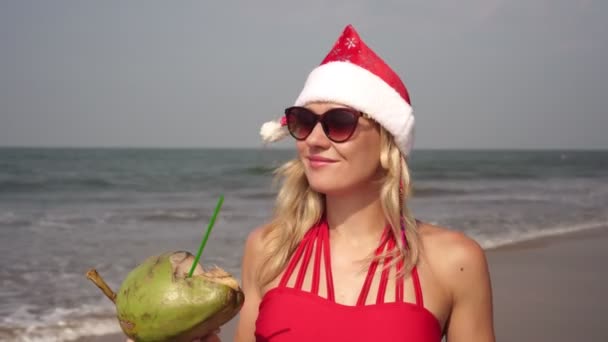 Noel Baba şapkasıyla sahilde güzel bir genç kadın. — Stok video