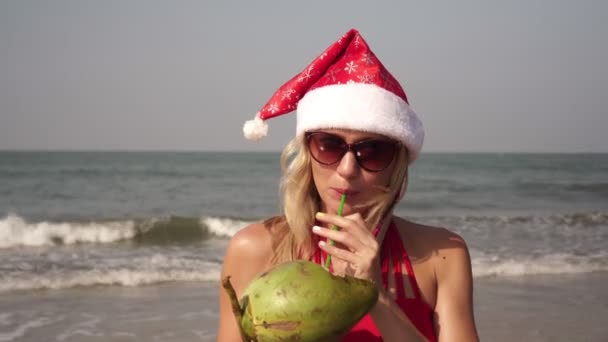 Noel, kumsalda kırmızı bikinili güzel kadın hindistan cevizli. — Stok video