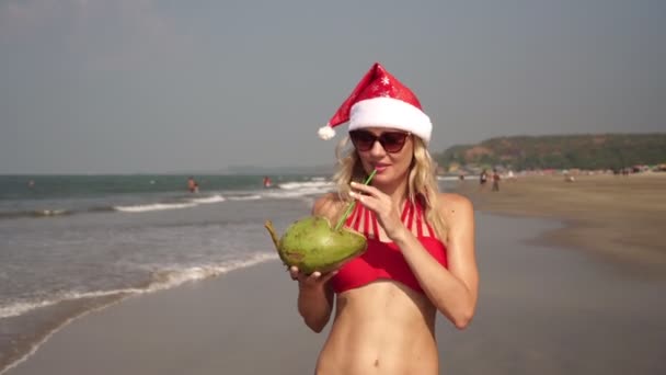 Krásná žena v červených bikinách na pláži slaví Vánoce v novoroční klobouku — Stock video