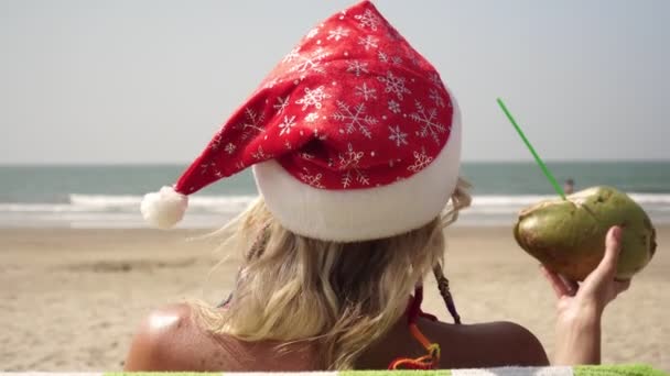 Una donna prende il sole su una spiaggia con un cappello da Babbo Natale. Capodanno e Natale al mare — Video Stock