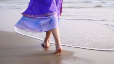 Doğulu elbiseli bir kadın deniz kıyısında yürüyor. Bacaklarını kapat.