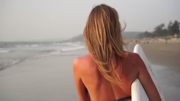 Giovane bella donna in bikini cammina lungo la spiaggia con una tavola da surf — Video Stock